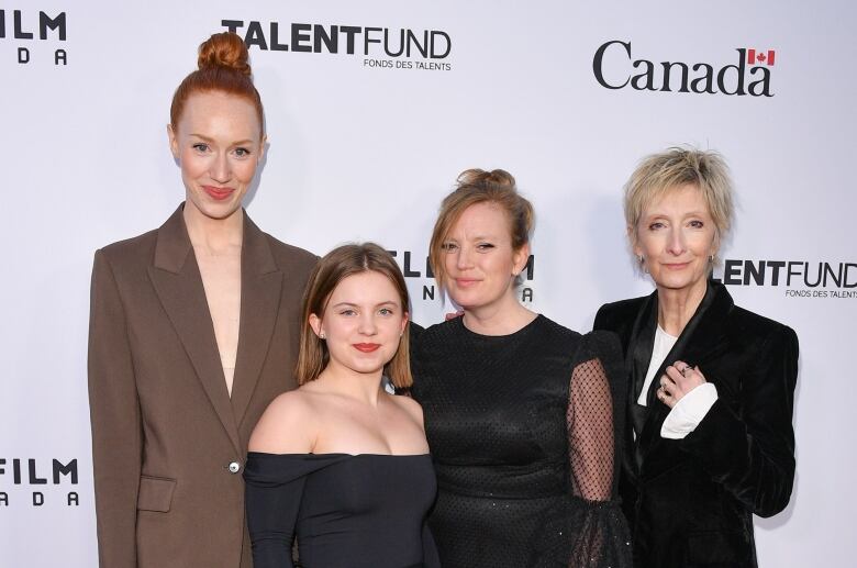 Four women dressed in formal wear pose on a red carpet.