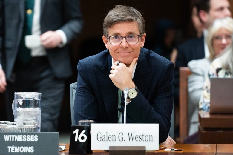 Galen Weston, in a blue suit and glasses, is shown seated at a table with a name card in front of him as he testifies about food inflation at a committee in Ottawa on March 8.