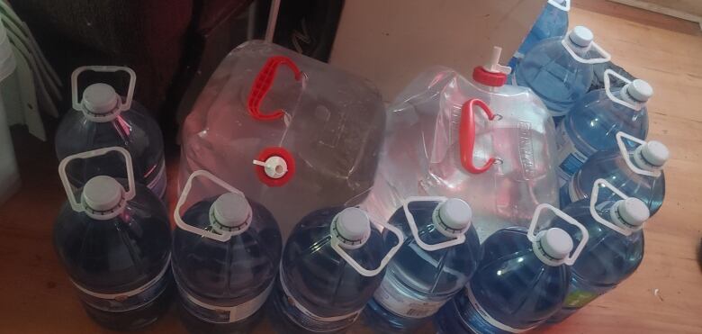 Two large bags of water surrounded by 10 jugs of water on a kitchen floor.