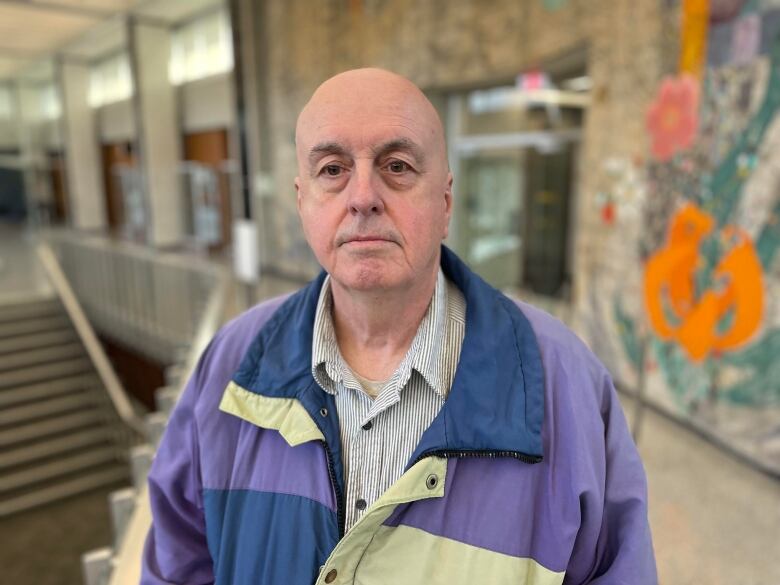 Man in striped shirt and windbreaker stands in front of a mosaic in Hamilton city hall.