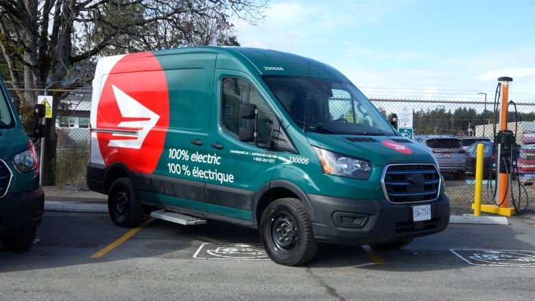 teal green electric mail delivery truck is parked in a parking lot. 