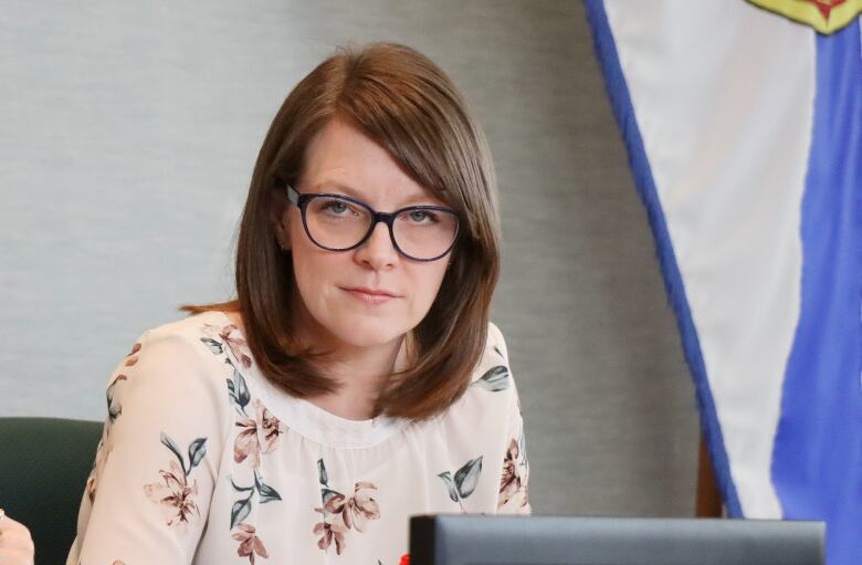 A woman looks directly at the camera with a Nova Scotia flag in the background.