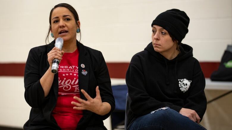 A woman sits speaking into a microphone she is holding.