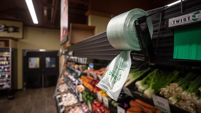 A roll of plastic produce bags hangs above produce at a grocery store.