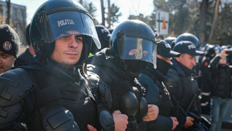 Riot police lock arms and form a line.