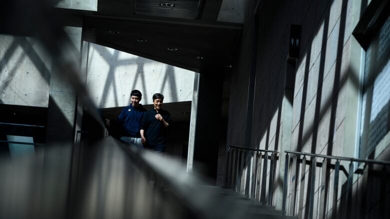 Two people walk up a large hallway in an art gallery with a mix of shadows and natural light.