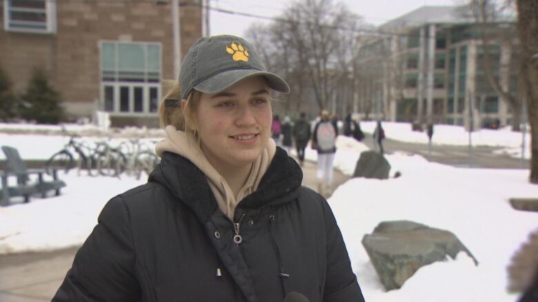 A woman wearing a cap standing outside a university. 