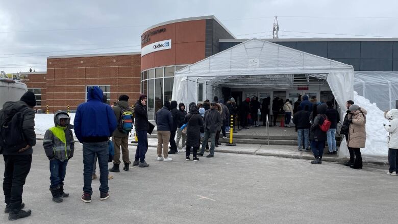 A long lineup of people stand outside an SAAQ service centre. 