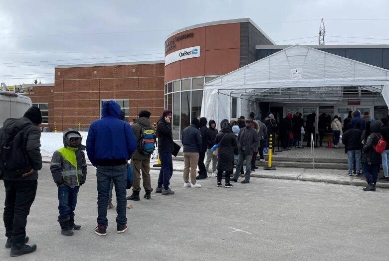 A long lineup of people stand outside an SAAQ service centre. 