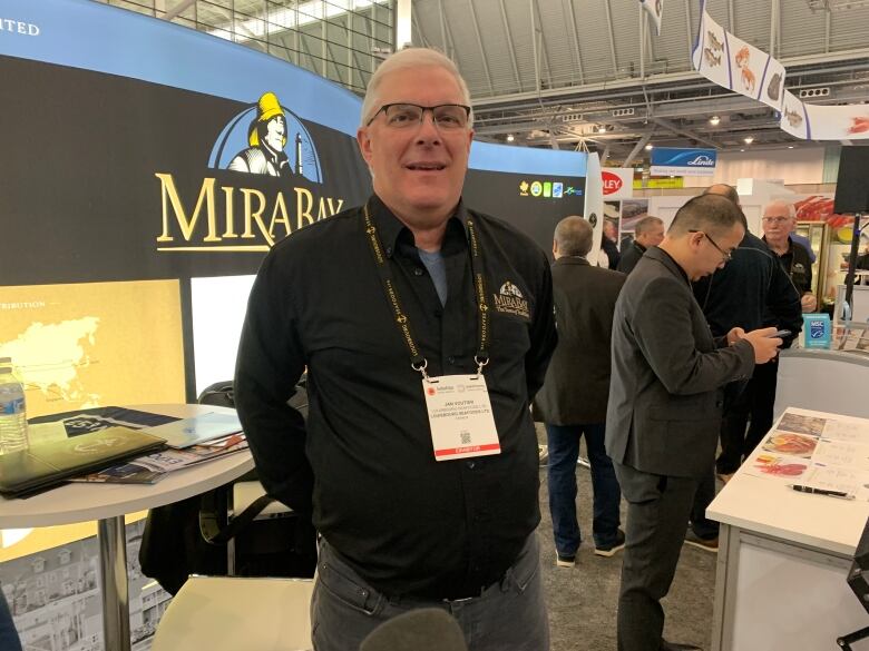 A man wears a lanyard and stands in front of a MiraBay backdrop. 