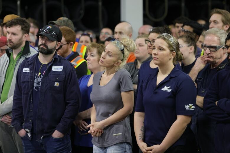 A crowd of people wearing Michelin uniforms stand listening to someone off camera.