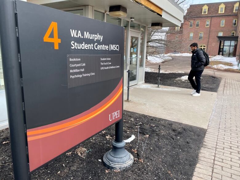 A UPEI student wearing a black winter coat and backpack walks into the university's student centre