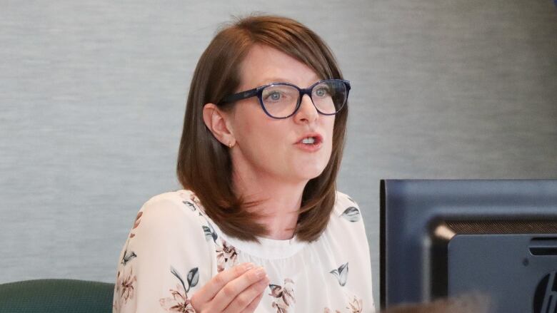 A woman with glasses and a flower print dress speaks out.