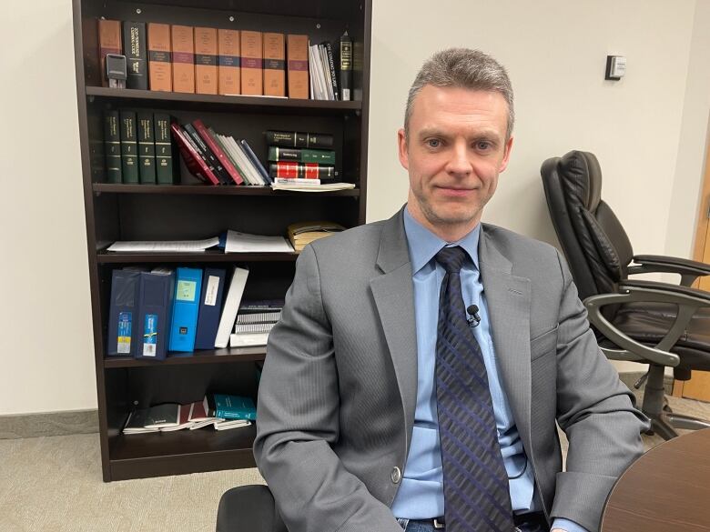 A man, wearing a suit and tie, sits in his office.