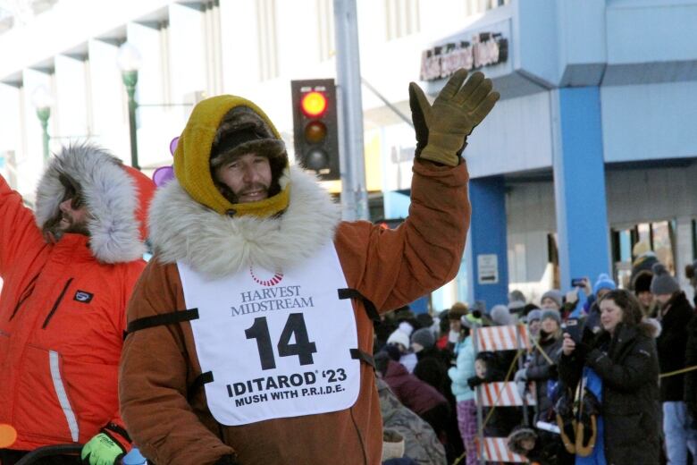 A man in a parka and numbered bib waves to a crowd of people.