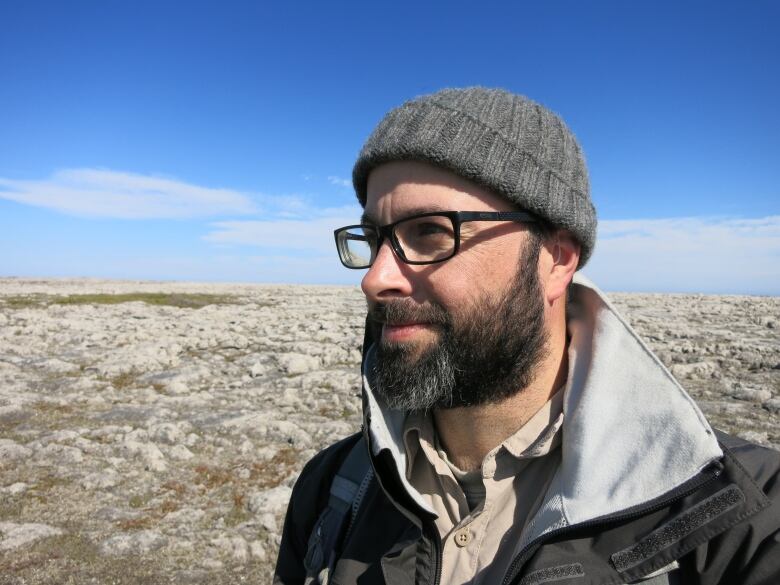 A man stands on a stony coastline.