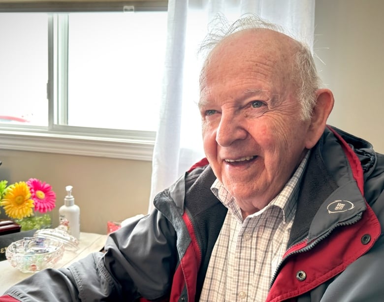 A man in front of a window smiles and talks to people off camera.