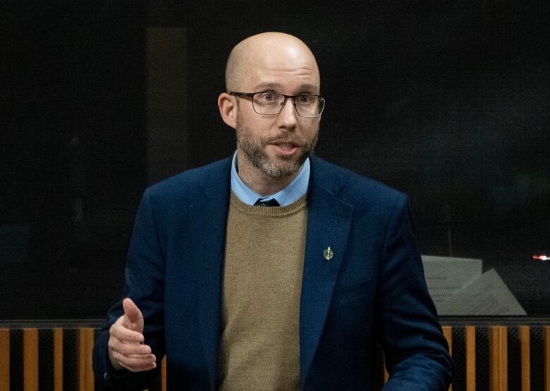 Man with glasses gestures while speaking in the House of Commons.