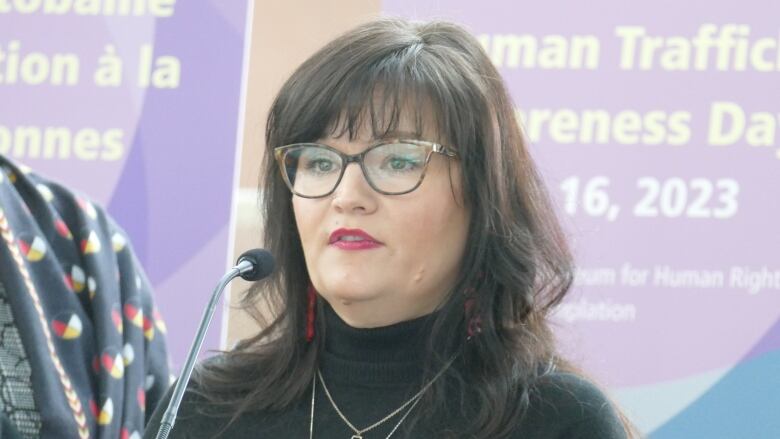 Women with brown hair and bangs stands in front of microphone wearing a black turtleneck and red lipstick .