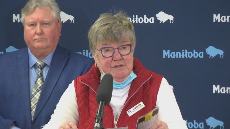 A woman with glasses and short hair speaks into a microphone.