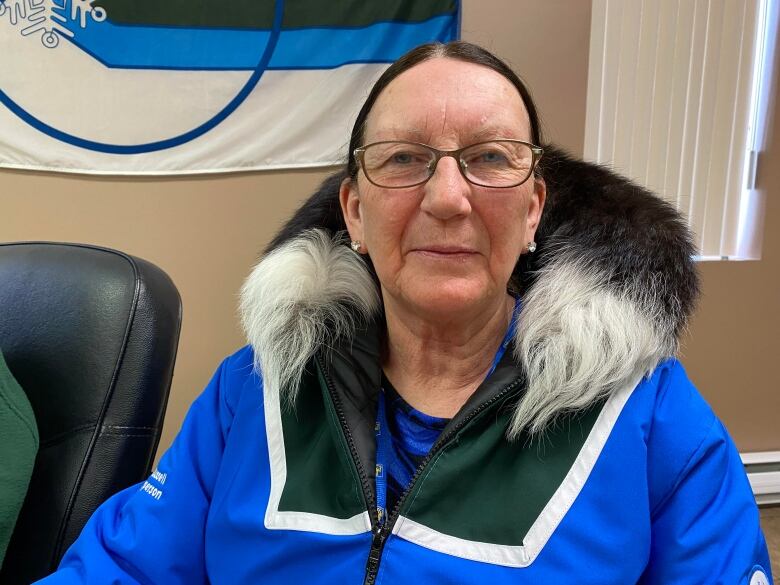 A woman wearing a blue, green and white organizers coat sits in an office chair.