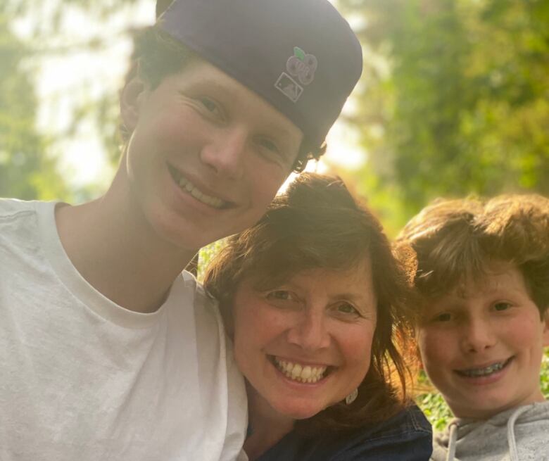 A smiling woman is standing between two boys. She is hugging the taller boy on the left. Both boys are smiling.