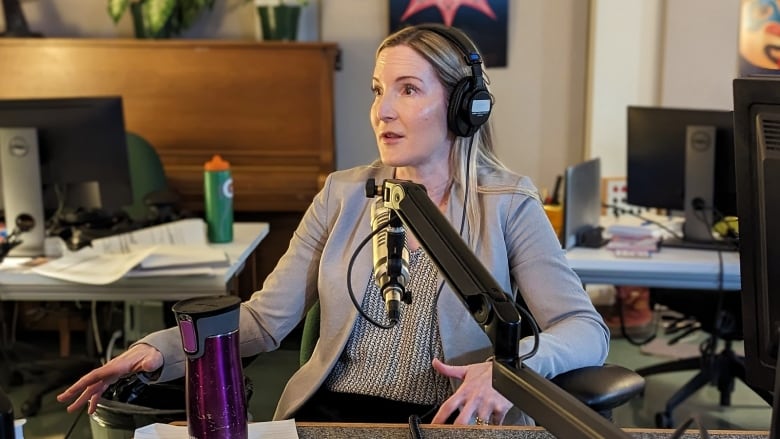 A woman sits at a microphone in a radio studio.