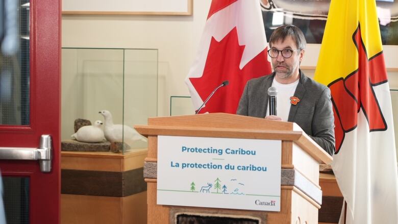 A scruffy man at a lectern speaks into a microphone.