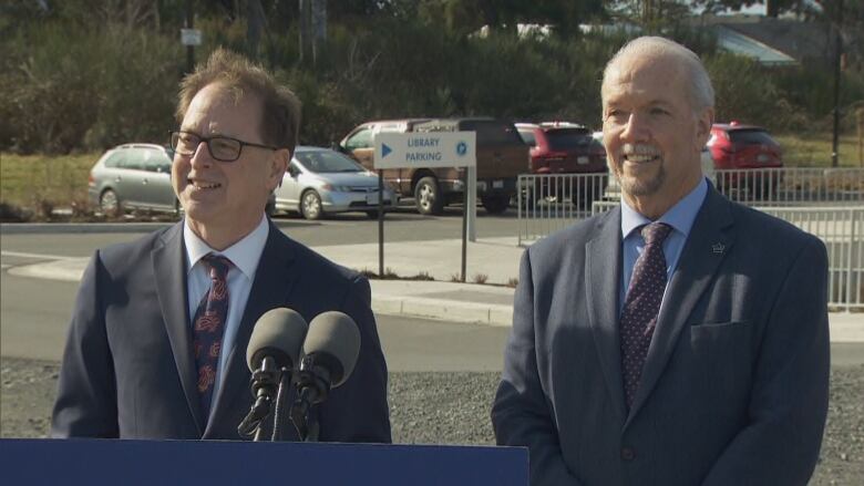 Two smiling men in suits stand at a microphone.