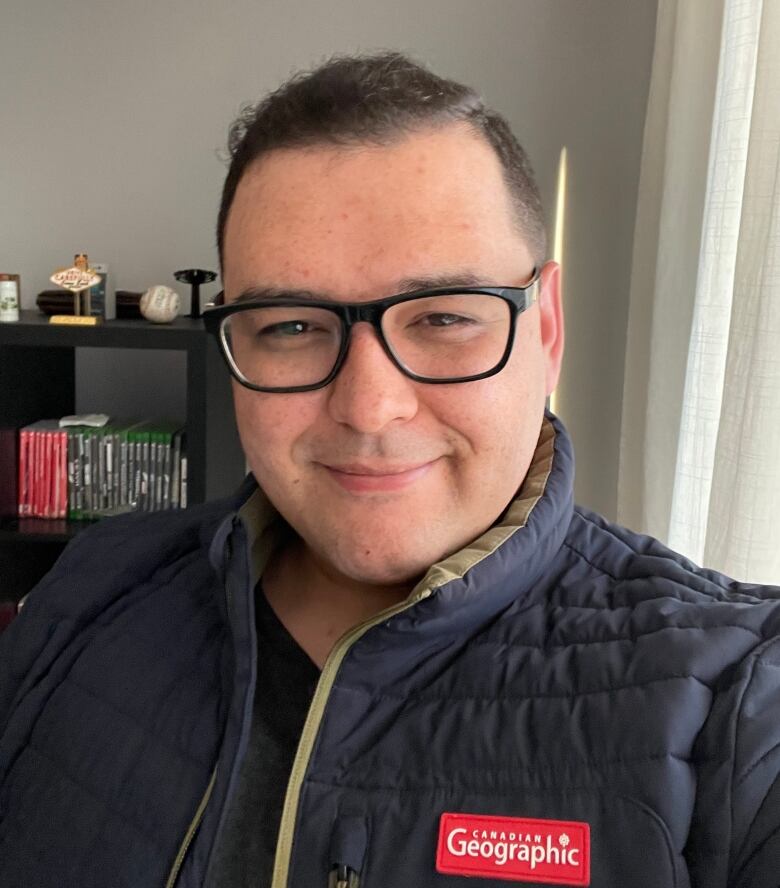 A man taking a selfie, wearing black framed glasses and a Canadian Geographic jacket.