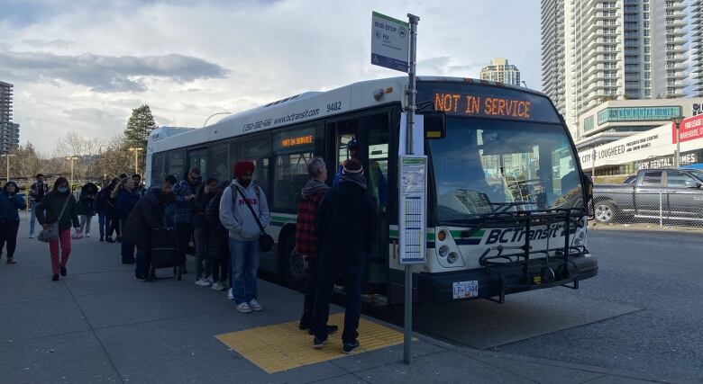 People line up and board a bus at a stop.