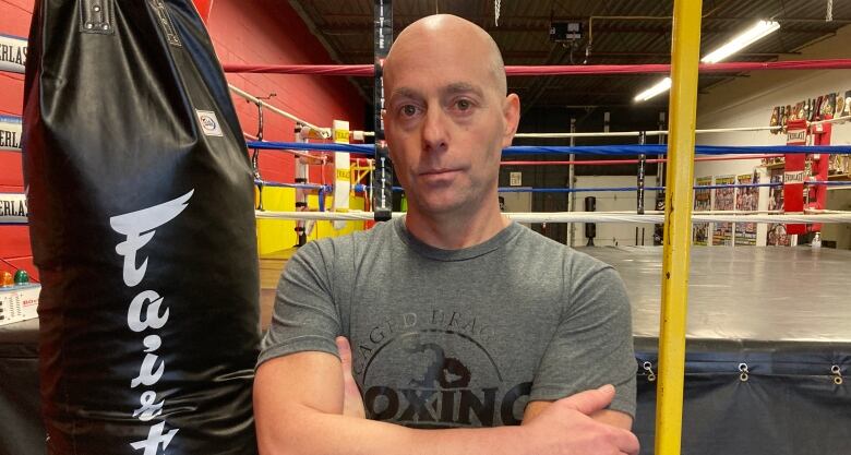 A former boxing official poses next to a ring and punching bag.