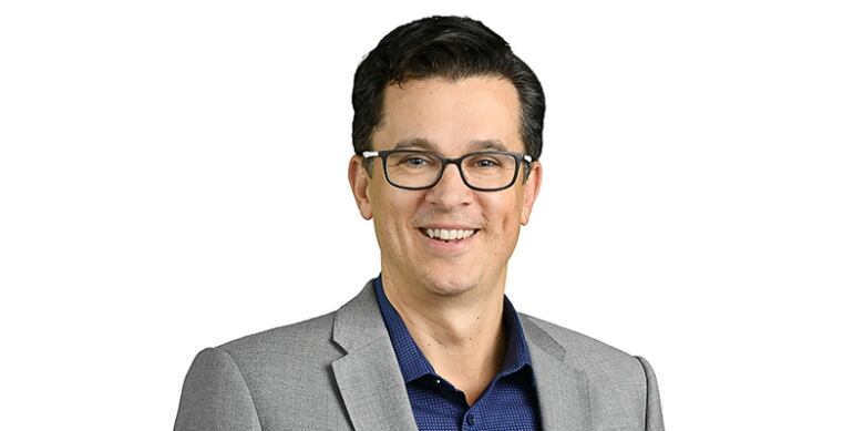 A man wearing a grey blazer standing in front of a white background