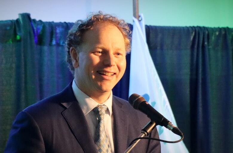 A man smiles and speaks into a microphone.