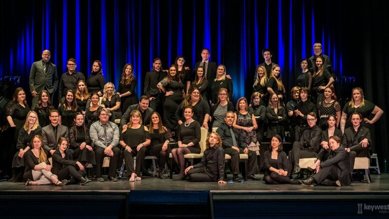 A large choir group poses on a stage.