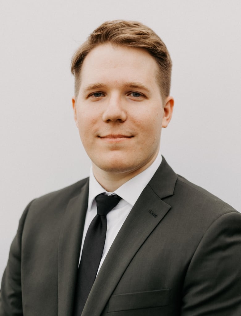 A man clad in a black suit and tie smiles.