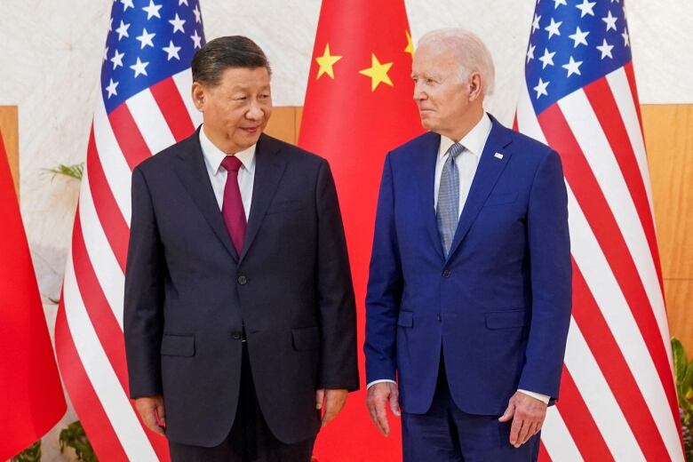 U.S. President Biden stands next to Chinese President Xi in front of flags.