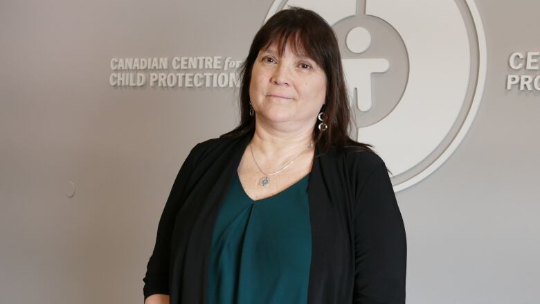 A woman smiles slightly in front of a wall with the words 'Canadian Centre for Child Protection' on it.