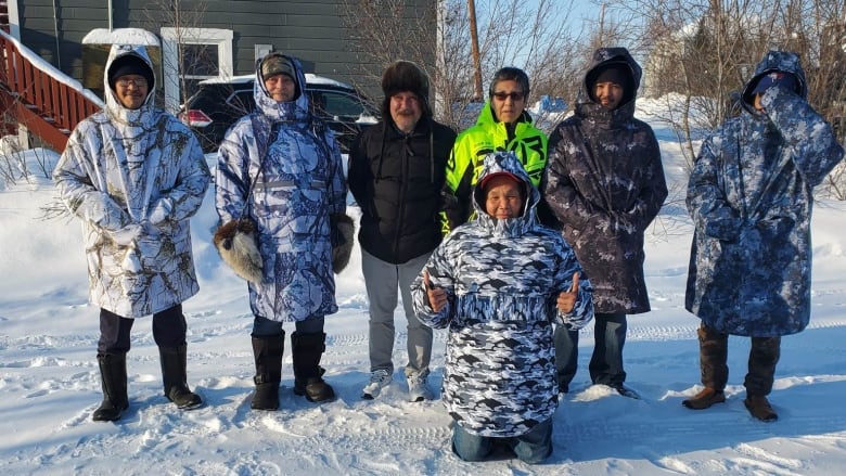 A line of men wearing parkas in the snow.