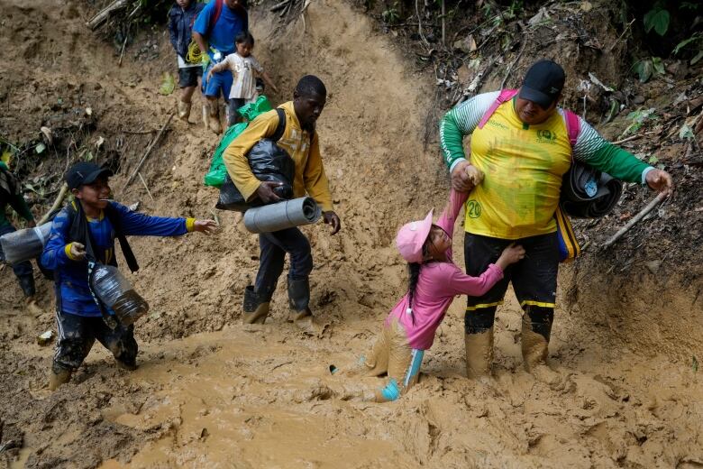 An Ecuadorian father helps his daughter traverse the mud in the Darien Gap as they walk from Colombia into Panama, hoping to eventually reach the U.S., on Oct. 15, 2022.