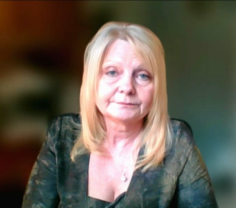 A middle-aged woman with long, blond hair sits in front of a blurred background.