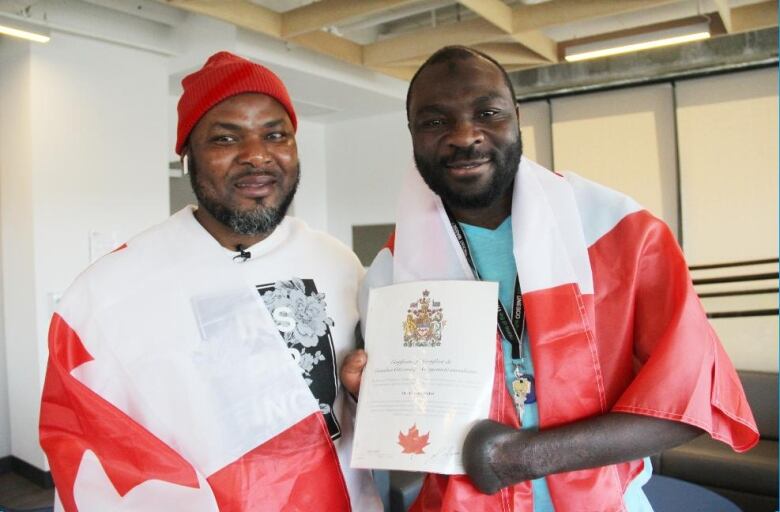 Razak Iyal, left, and Seidu Mohammed pose together for a photo. Mohammed is holding his certificate of Canadian citizenship, while they're both draped with Canadian flags behind their back.