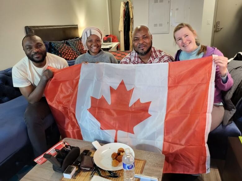 Four people, Seidu Mohammed, Mariam _______, Razak Iyal and Laurel Martin, are sitting on a blue couch and holding a Canadian flag.