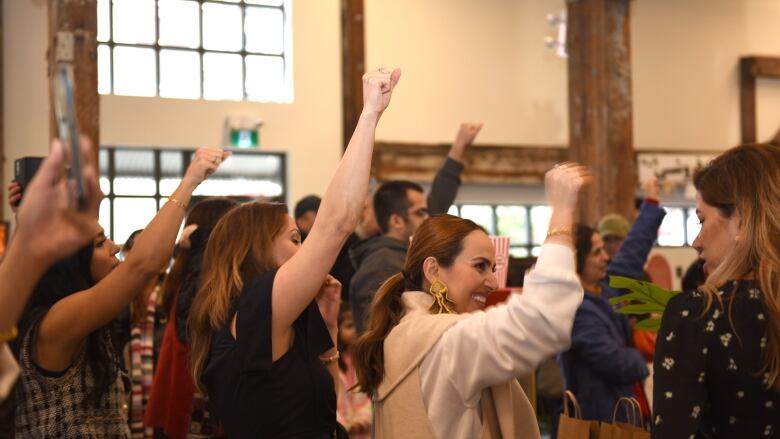 A crowd of women and men are pictured indoors with their fists held high. 