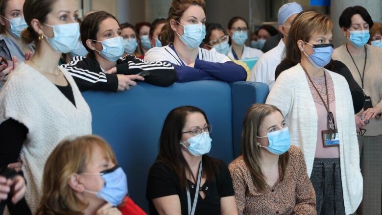 People in face masks watch a news conference.