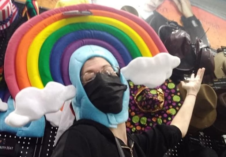 A woman wearing a mask and a hat with a cloud and rainbows around it.