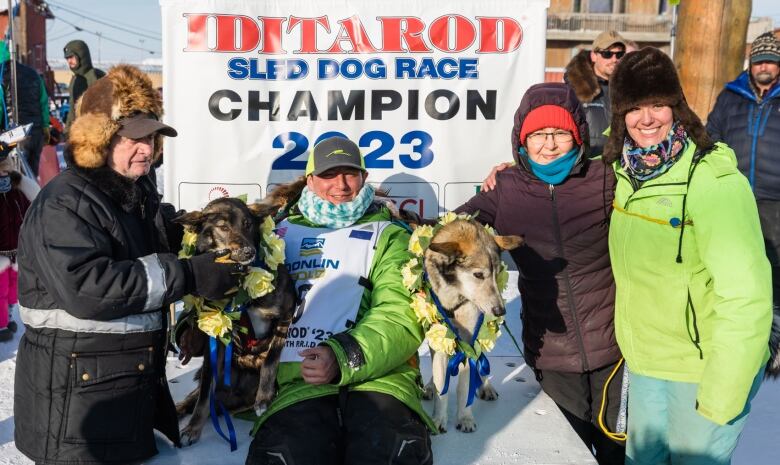 A family smiles taking a photo together with their lead sled dogs. A boisterous crowd looks on.