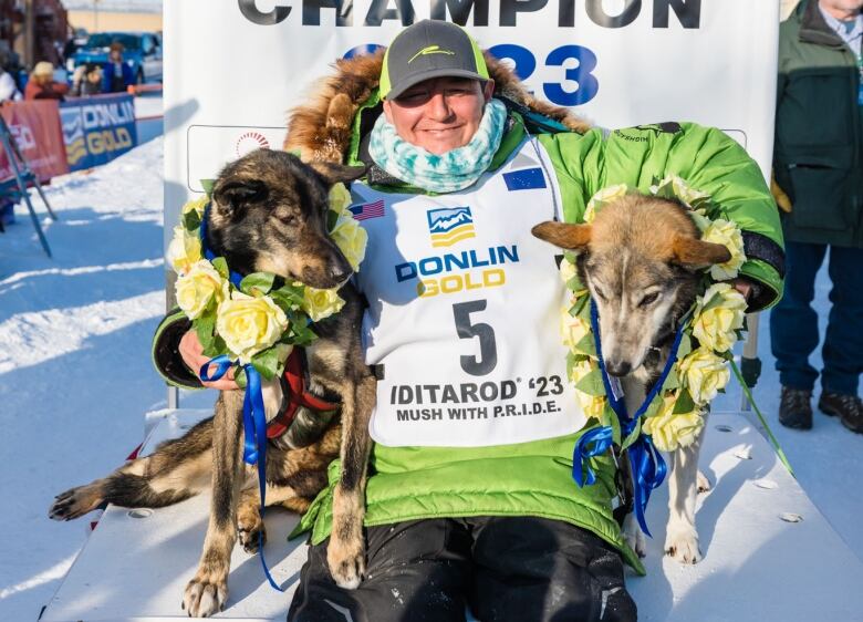 Winners of The Iditarod dog sled race pose for a photo beneath the sign that reads 'Iditarod Dog Sled Race Champion 2023.'