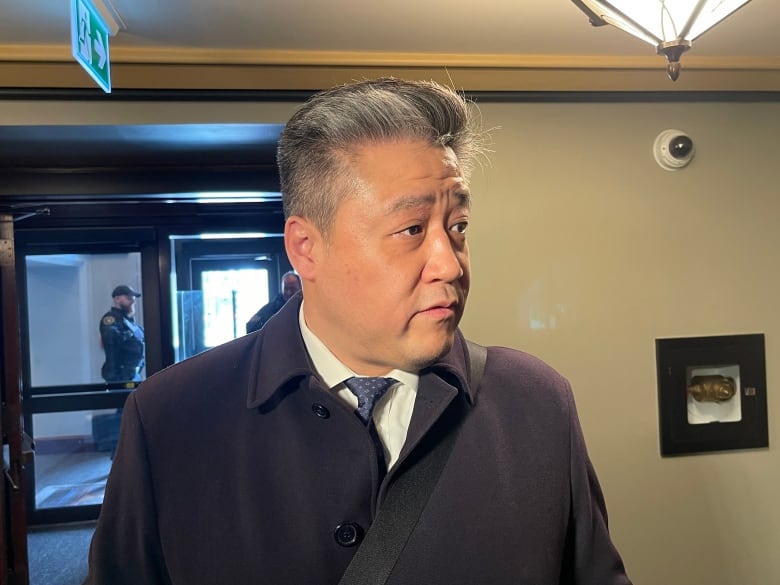 A man in a jacket, shirt and tie stands in a hallway.