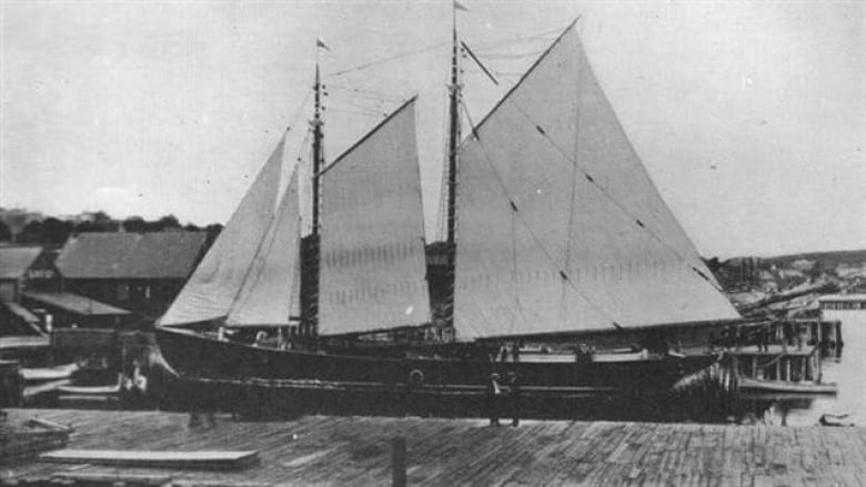 An old black-and-white photo of a large schooner with white sails.